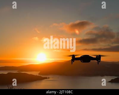 Bei Sonnenuntergang schwebt die Drohne über dem Meer vor der Kulisse der Berge Stockfoto