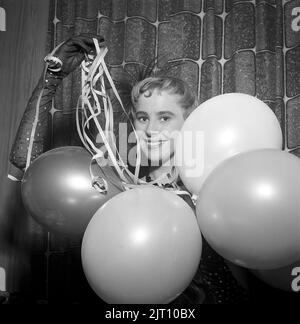 Party in der 1950s. Eine junge Frau hält Ballone und Konfetti und blickt lächelnd in die Kamera. Schweden 1955 Stockfoto