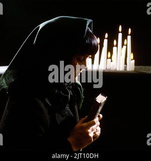 Kirche in der 1970s. Eine Frau fotografiert wie in einer Kirche mit brennenden Kerzen im Hintergrund. Sie hält ein abgenutztes Psalmenbuch oder die bibel in ihren Händen. Schweden Stockfoto