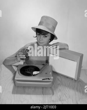 1960s Lifestyle. Eine junge Frau mit einem Philips Radio und einem Grammophon, wie es im Sommer aussehen könnte. Der Sommerhut und das kühle Trinkglas sind im Bild, um das richtige Sommergefühl zu bekommen. Schweden 1960s Foto Kristoffersson Ref 374A Stockfoto