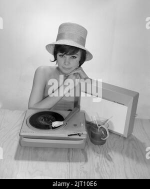 1960s Lifestyle. Eine junge Frau mit einem Philips Radio und einem Grammophon, wie es im Sommer aussehen könnte. Der Sommerhut und das kühle Trinkglas sind im Bild, um das richtige Sommergefühl zu bekommen. Schweden 1960s Foto Kristoffersson Ref 374A Stockfoto