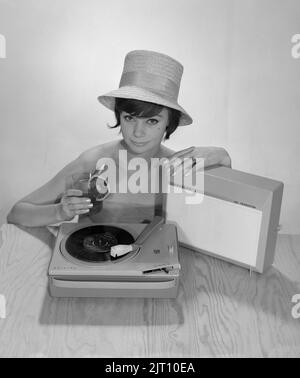 1960s Lifestyle. Eine junge Frau mit einem Philips Radio und einem Grammophon, wie es im Sommer aussehen könnte. Der Sommerhut und das kühle Trinkglas sind im Bild, um das richtige Sommergefühl zu bekommen. Schweden 1960s Foto Kristoffersson Ref 374A Stockfoto