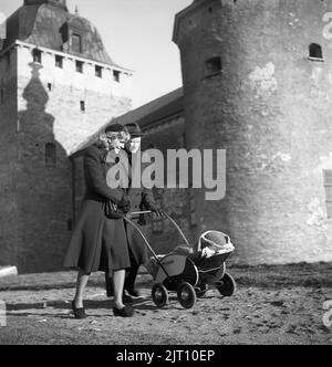 Eltern in den 1940s. Eine stolze Mutter und ein stolzer Vater gehen mit ihrem Kind im Kinderwagen. Der Babywagen hat ein typisches Design aus dem Jahr 1940s mit einem Holzkörper, der in Schwarz und Weiß lackiert ist. Kalmar Sweden 1945 Kristoffersson Ref. R110-4 Stockfoto