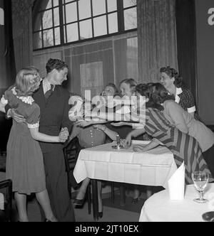 In der 1940s. Sieben junge Frauen, aber nur ein Mann, und die sechs, die nicht tanzen, strecken ihre Arme für ihn aus. Das Bild wurde in der Stadt Boras aufgenommen, wo es heißt, dass es einen Mangel an Single-Männern gibt. Nur ein freier und alleinerziehender Mann auf sieben Frauen. Schweden 1942. Foto Kristoffersson Ref. A50-3 Stockfoto