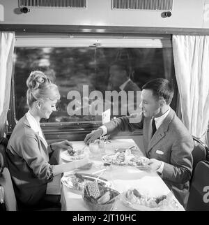 Zugfahrt in der 1960s. Ein Paar im Restaurantwagen des Zuges genießt das gemeinsame Abendessen. Sie hat eine typische Frisur von 1960s. Schweden 1960s Kristoffersson Ref. DD107-4 Stockfoto