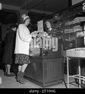 Einkaufen in der 1940s. Eine junge Frau in einem Geschäft, in dem eine Verkaufsfrau einige der Geschäfte mit warmen Handschuhen und Fäustlingen präsentiert. Schweden 1947. Kristoffersson Ref. Y71-4 Stockfoto