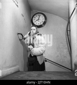 In der 1950s. Eine Frau ist sichtbar erschöpft, wenn sie die Treppe hinauf läuft, vielleicht ist sie ein paar Minuten zu spät für ihren Termin um acht Uhr, da die Uhr an der Wand zeigt, dass es ein paar Minuten vorbei ist. Schweden 1950 Kristoffersson Ref. AX7-1 Stockfoto