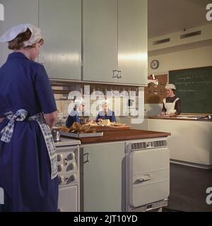 In der Küche 1960s. Das Innere einer Küche in einer Schule, die für Kochkurse genutzt wird. Mädchen und ihre Lehrerin sind in Schürzen gekleidet. Schweden 1962 Ref. CV17-11 Stockfoto