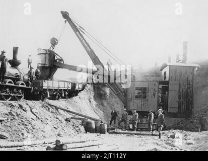 Bau von Eisenbahnen. Eine Szene aus Südschweden und der Bohus-Eisenbahn, die zu Beginn des 20.. Jahrhunderts gebaut wird. Der Großbagger ist aus deutscher Sprache hergestellt und mit Dampf betrieben. Eine hausähnliche Kabine passt zur Dampfmaschine und den Menschen, die sie manövrieren. Die Erde und die Felsen werden auf Eisenbahnwaggons für den Transport verladen. Die Arbeit ist zum Stillstand gekommen, als der Fotograf das Bild aufgenommen hat. Stockfoto