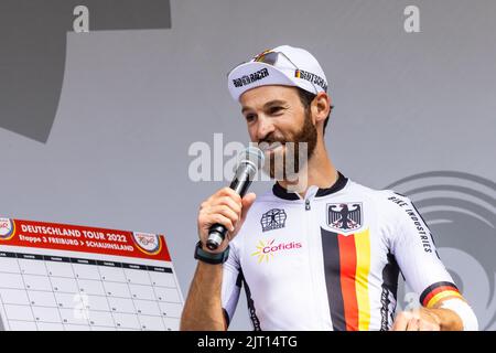 Freiburg Im Breisgau, Deutschland. 27. August 2022. Simon Geschke steht vor der dritten Etappe der Deutschlandtour in Freiburg am Start und spricht ins Mikrofon. Die 3. Etappe der Deutschland-Rundfahrt führt von Freiburg über den Breisgau und das Markgräfler Land ins Schauinsland. Quelle: Philipp von Ditfurth/dpa/Alamy Live News Stockfoto