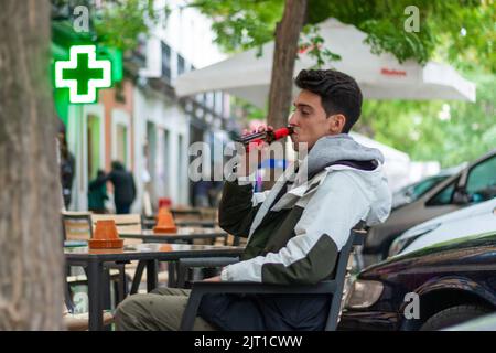 Schöner maskuliner Mann mit einem Mantel, der draußen an einem Restauranttisch sitzt und Bier trinkt Stockfoto