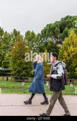 Zwei schöne Freunde, ein Mann und eine Frau, die in einem grünen Park spazieren. Es Ist Herbst Stockfoto