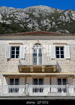 Budva, Montenegro - 22.08.22: Steinfassade des Gebäudes mit durchbrochenen Balkonen vor der Kulisse der Berge Stockfoto