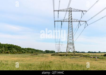 An einem teilweise bewölkten Sommertag unterstützen Strommasten Hochspannungsleitungen auf dem Land Stockfoto