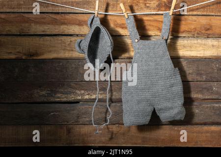 Babykleidung, aufgehängt an einer Wäscheleine mit Holzhaken, Overalls und Hut. Kleidung trocknet im Schatten. Kopierraum. Reinigungskonzept. Hand häkeln k Stockfoto