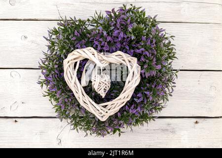 Handgemachte Deko-Kranz aus trockenen Holzzweigen, Stäbchen und Blumen, die an der weißen Holzwand hängen Stockfoto