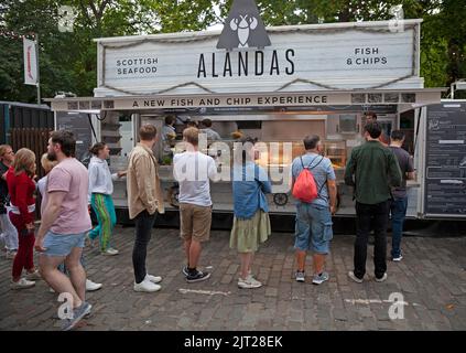 Edinburgh City Centre, Schottland, Großbritannien. 27. August 2022. Geschäftiges Abschlusswochenende des Edinburgh Festival Fringe, Temperatur 18 Grad, sehen Sie die Straßen voller Menschen aller Art, die die lebhafte Atmosphäre genießen. Leute in der Schlange für Fisch und Chips am George Square. Quelle: Arch White/Alamy Live News Stockfoto