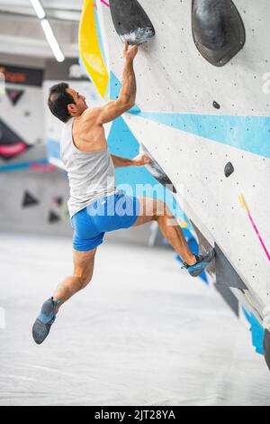 Ein starker Mann klettert an der Wand in der Kletterhalle Stockfoto