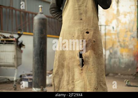 Alte Schürze. Arbeitskleidung. Zerrissenes Stück Tuch. Schürze in Löchern. Details der Arbeiten in der Garage. Stockfoto