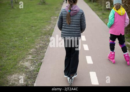 Kind auf Rollerrollen im Park. Kind auf dem Roller. Spaziergang mit Kindern in der Stadt. Radweg aus Asphalt. Stockfoto