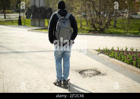 Kerl fährt Roller, Kerl fährt um die Stadt auf Roller. Mann mit Rucksack auf der Straße. Stockfoto