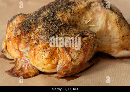 Das ganze Huhn ist mit gemischten Kräutern überzogen und im Ofen geröstet. Auf einem braunen Papierhintergrund Stockfoto