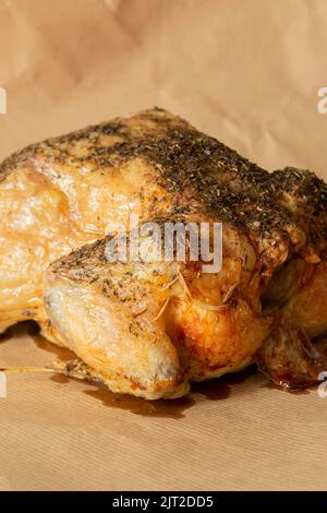 Das ganze Huhn ist mit gemischten Kräutern überzogen und im Ofen geröstet. Auf einem braunen Papierhintergrund Stockfoto