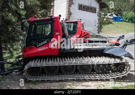 Ein roter PistenBully 600 W Pistengroomer parkte an einem sonnigen Tag in der Nähe eines grünen Baumes und eines Gebäudes Stockfoto