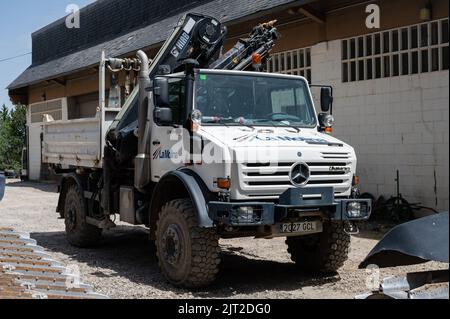 Ein weißer Mercedes Benz Unimog G5000 Geländewagen mit einem Kran, der in der Nähe eines Gebäudes geparkt ist Stockfoto