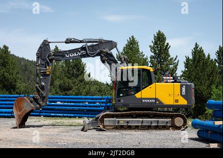 Seitenansicht eines großen gelb-schwarzen Volvo EC160E Baggers mit einem Eimer auf einer Baustelle in der Nähe von Bäumen Stockfoto