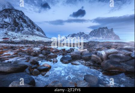 Küste mit Steinen und verschwommenem Wasser, schneebedeckten felsigen Bergen Stockfoto