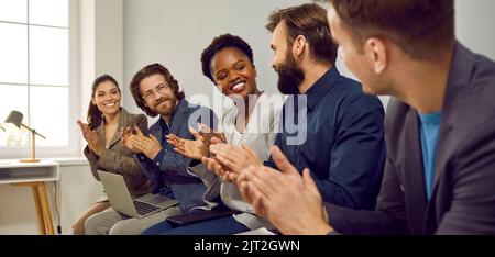 Glückliches Team, das dem Kollegen nach einer Geschäftspräsentation bei einem Arbeitsgespräch Anerkennung zeigt Stockfoto