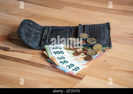 Eine schwarze Geldbörse mit Euro-Banknoten und Münzen, die auf einer hölzernen Oberfläche platziert sind Stockfoto