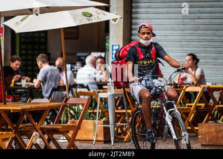 Junger Mann, der in der Nähe eines belebten Restaurants in Savassi in Belo Horizonte, Brasilien, mit dem Fahrrad unterwegs ist. Stockfoto