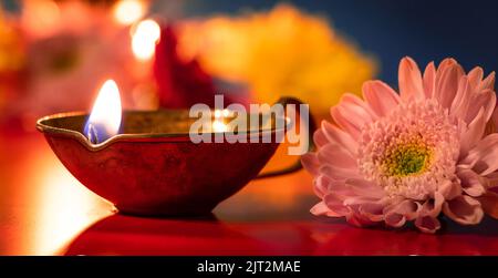 Frohes Diwali. Traditionelles indisches Festival des Lichts. Brennende Diya-Öllampen und Blumen auf rotem Hintergrund. Bannerformat. Stockfoto