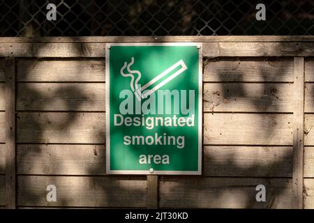 Ein grünes Schild auf einem Holzzaun mit der Aufschrift Raucherbereich im Freien Stockfoto
