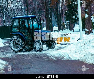 Blauer Traktor reinigt Stadtstraßen und Straßen nach starkem Schneefall. Kommunale Dienste sind an der Schneeräumung beteiligt. Stockfoto