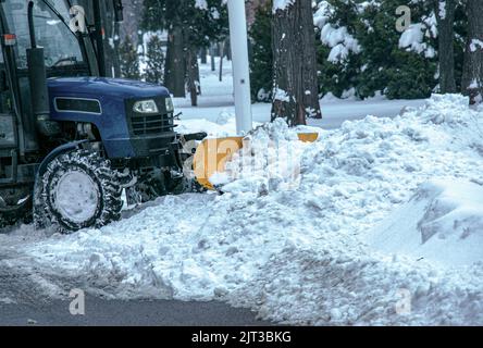 Blauer Traktor reinigt Stadtstraßen und Straßen nach starkem Schneefall. Kommunale Dienste sind an der Schneeräumung beteiligt. Stockfoto