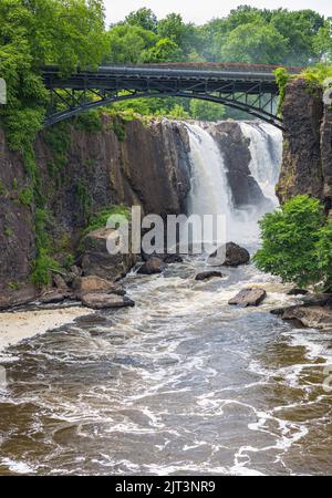 Eine wunderschöne Aussicht auf den Pherson Great Falls National Historical Park mit einer Brücke über das fließende Wasser, umgeben von üppigem Grün Stockfoto