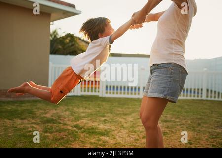 Die besten Tage sind, wenn wir spielen. Eine Mutter schwingt ihren Sohn spielerisch in ihrem Hinterhof herum. Stockfoto