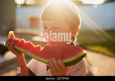 Süßer Geschmack des Sommers. Ein entzückender kleiner Junge, der eine Scheibe Wassermelone im Hinterhof isst. Stockfoto