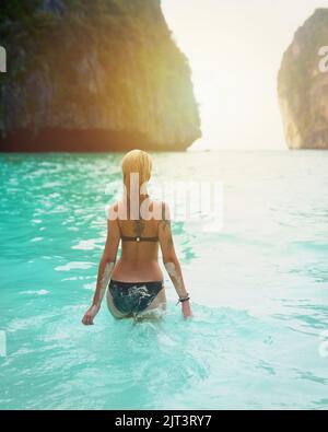 Die Art von Urlaub, von der die meisten nur träumen. Rückansicht einer schönen jungen Frau in einem Badeanzug, die in den Ozean geht. Stockfoto