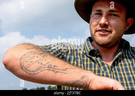 Mainz, Deutschland. 19. August 2022. Der Wanderhirte Finn-Ole Stephan zeigt auf seinem Arm eine Tätowierung mit der Aufschrift "Schäfer". Zusammen mit einem Eselpfleger ist er an einem Weideprojekt im Naturschutzgebiet Mainzer Sand beteiligt. (To dpa: 'Schafe und Esel als Naturschützer - Tierhalter brauchen Unterstützung') Quelle: Peter Zschunke/dpa/Alamy Live News Stockfoto