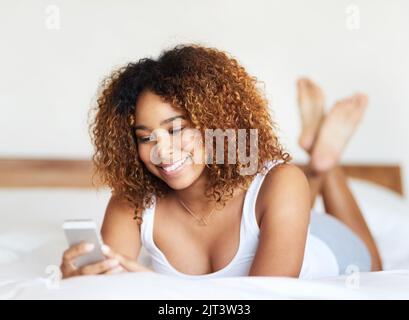 Es gibt nichts Schöneres als einen süßen Morgentext. Eine junge Frau schreibt auf ihrem Bett. Stockfoto
