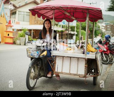 Lust auf etwas Süßes unterwegs? Porträt einer jungen Lebensmittelverkäuferin, die an ihrem Stand in Thailand wartet. Stockfoto