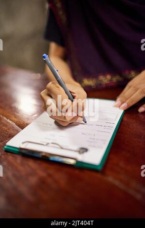 Einchecken im Hotel. Nahaufnahme einer Frau, die ein Hotel-Check-in-Formular auf einem Clipboard an einem Hotelrezeptionsschalter ausfüllt. Stockfoto