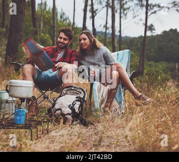 Abenteuerlustiges junges Paar, das sich auf einem Stadtplan ansieht, während es auf ihrem Campingplatz sitzt. Glückliches junges Paar, das im Wald zeltet. Stockfoto