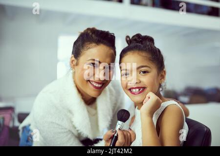 Ich und meine kleine Schönheitskönigin. Porträt einer Mutter und ihres niedlichen kleinen Mädchens, das sich in einer Garderobe zusammen schminkt. Stockfoto