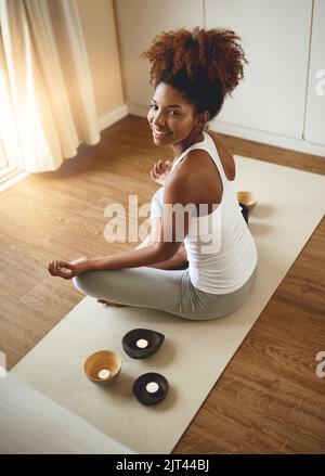 Meine Chakren ausrichten. Hochwinkelporträt einer sportlichen jungen Frau, die in Innenräumen Yoga praktiziert. Stockfoto