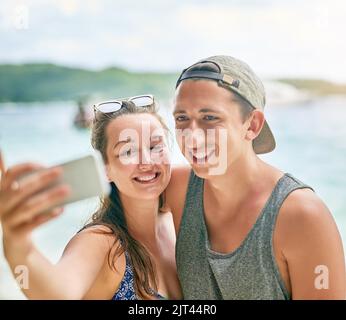 Selfies am Strand sind ein muss. Ein glückliches Paar, das ein Selfie am Strand macht. Stockfoto